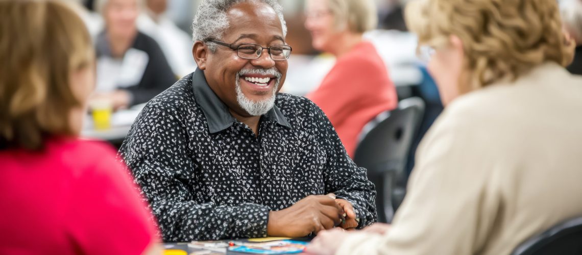 A diverse group of seniors laugh and socialize while playing a board game in a welcoming daycare center filled with natural light and colorful decorations.