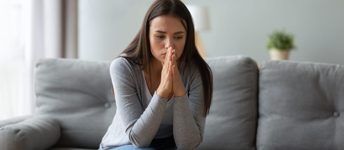 Pensive millennial girl sit on sofa in living room look in distance thinking or pondering of problem, thoughtful young woman lost in thoughts feel frustrated or distressed at home, drama concept