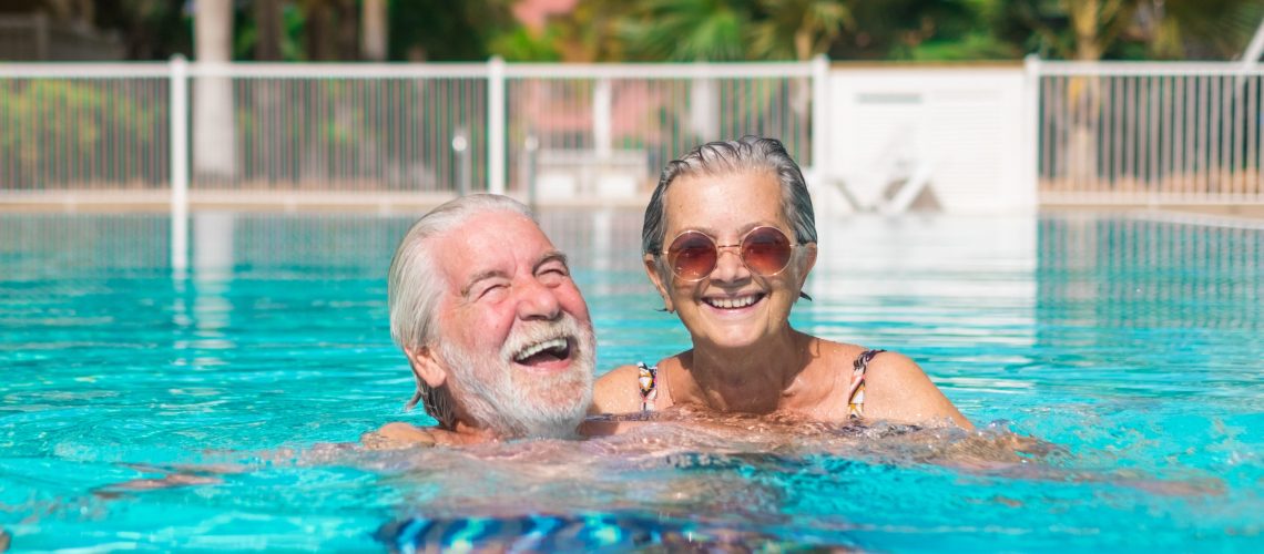 Couple of two happy seniors having fun and enjoying together in the swimming pool smiling and playing. Happy people enjoying summer outdoor in the water